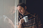 Sad man by window drinking coffee