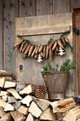 Garland of fir cones on wooden shutter above stacked firewood