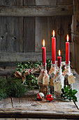 Mit Kräutern gefüllte Flaschen als Kerzenständer auf rustikalem Holzuntergrund