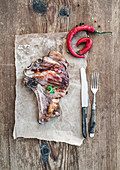 Ribeye Steak mit Chilischote auf Papier und Holzuntergrund (Aufsicht)