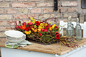Rot-gelbes Tischgesteck mit Tulpen, Narzissen und Ranunkeln auf Moos und Zweigen