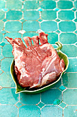 A raw rack of lamb in a leaf shaped bowl