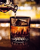 Cocktail in Glas mit Eiswürfeln gießen