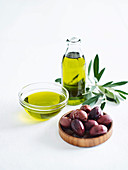Olivenöl in Flasche und Schale, davor Oliven