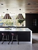 Elegante Kücheninsel mit Marmor-Arbeitsplatte, Barhocker und Hängelampen in offenem Wohnraum