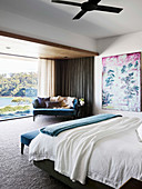 Doppelbett, Gemälde und blaues Sofa in großzügigem Schlafzimmer mit Glasfront
