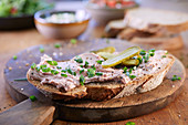 A slice of bread spread with liver pâté and topped with chives and gherkins