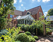 Brick house with conservatory surrounded by garden with fence