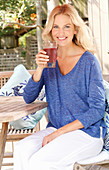 Blonde Frau in blauem Shirt und weißer Hose mit einem Drink