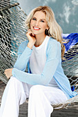 Blonde Frau in weißem Top und hellblauer Jacke sitzt in der Hängematte