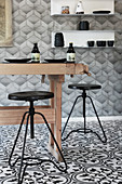 Rustikaler Holztisch und schwarze Hocker in Küche mit schwarz-weißen Ornamentfliesen