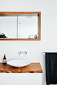 Designer sink on washstand with wooden top below wood-clad niche with mirror on back wall