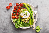 Toast with avocado cream and a poached egg served with tomatoes, spinach and asparagus