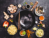 An arrangement of a wok and ingredients for an oriental noodle dish (seen from above)