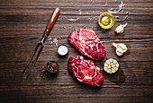 Zwei rohe Ribeye-Steaks auf Holzuntergrund (Aufsicht)