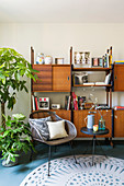 Chair and side table in front of retro shelving and houseplant