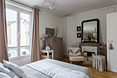 Double bed, chest of drawers and disused fireplace in bedroom in natural shades