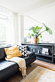 Black leather sofa next to half-height cabinet in bright living room