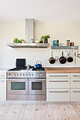 Modern gas cooker below extractor hood and hook rail in bright kitchen