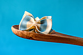 Farfalle with blue stripes on a wooden spoon in front of a blue background
