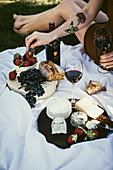 A cheese platter with strawberries, red wine, grapes and bread on a picnic blanket