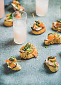 Party crostini with smoked salmon, pesto sauce, watercress and capers with pink grapefruit cocktails
