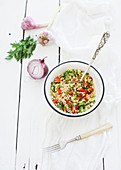 Healthy bulgur salad with paprika, red onion, parsley and garlic in rustic metal bowl. Vintage silverware, white wooden backdrop