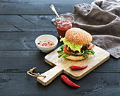 Fresh homemade burger on dark serving board with spicy tomato sauce, sea salt and herbs over dark wooden background