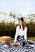 A young woman wearing an elegant white blouse and a printed skirt sitting on a picnic blanket