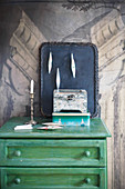 Tin, wooden box, black tray with Christmas baubles and candle on top of green chest of drawers