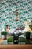 Grün-weiße Tapete mit Blumenmuster, runder Tisch mit weißer Keramik und Laternenleuchte
