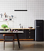 Schwarze Küchenzeile und schwarzer Kühlschrank vor Tapete mit Gittermuster, Esstisch und Stul