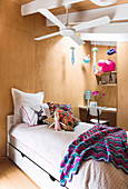 Bed under ceiling fan in girl's room with wooden paneling