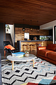 Ledercouch, Ledersessel und Marmor-Coffeetable auf Teppich, im Hintergrund Küche mit Holzfronten in offenem Wohnraum