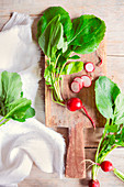 Radishes with leaves on a wooden board, whole and sliced