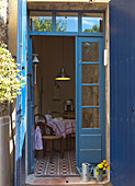 View through open French windows with blue-painted frame into kitchen-dining room