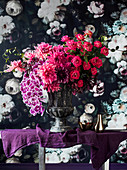 Opulent bouquet of flowers in an amphora in front of floral wallpaper