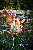 Flowers in wicker basket and baguette in floral shopping bag hung from bicycle