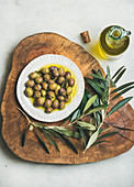 Eingelegte grüne Oliven und Zweige auf Olivenholzbrett