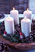 Vier Stumpenkerzen in Holzschale weihnachtlich dekoriert mit Moos, Zapfen und Zwergenfiguren
