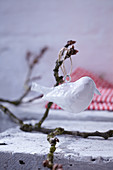 White bird ornament hung from branch as wintry garden decoration