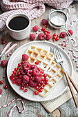 Waffles topped with red currants and raspberries served with cup of black coffee