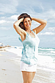 A brunette woman on a beach wearing shorts and a vest top