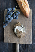 Blue cheese with oak leaves, a baguette, and a bunch of grapes