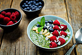 A breakfast bowl with spinach smoothie, raspberries, cashew nuts, blueberries and coconut flakes