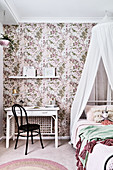 White desk and black chair next to child's bed with canopy in girl's bedroom with floral wallpaper