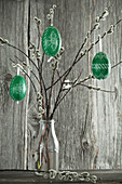 Green-painted Easter eggs hung from pussy willow branches in bottle