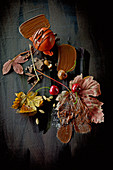 Food-Art: Winterapfel mit Schokolade, Kirschen und Herbstblättern auf schwarzem Untergrund