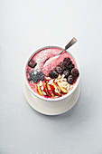 Fresh and cold strawberry banana smoothie garnished with peach slices, frozen blackberry, chia seeds and almond flakes