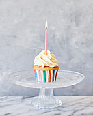 Ein Party-Cupcake mit Frosting und rosa Kerze auf Kuchenständer